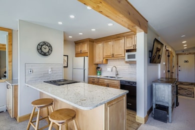 Kitchen featuring tasteful backsplash, light stone counters, black appliances, a kitchen bar, and recessed lighting