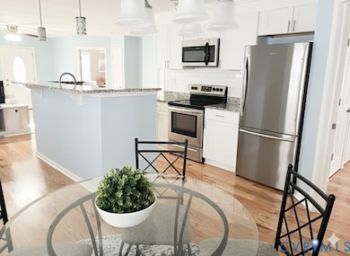 Kitchen featuring granite countertops,  stainless steel appliances, hanging light fixtures, a breakfast bar area, and hardwood-flooring