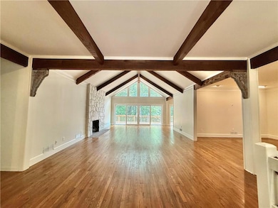 Unfurnished living room featuring wood finished floors, a stone fireplace, and baseboards