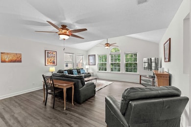 Living area with ceiling fan, dark wood finished floors, wall of windows.