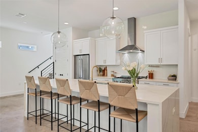 Kitchen with light stone counters, a kitchen bar, wall chimney range hood, white cabinetry, and a large island with sink