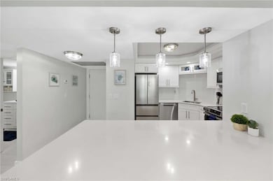 Kitchen with stainless steel appliances, white cabinetry, light countertops, decorative backsplash, and pendant lighting