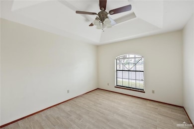 Unfurnished room with light wood finished floors, a ceiling fan, a raised ceiling, and baseboards