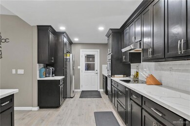 Kitchen with stainless steel refrigerator, light hardwood / wood-style floors, black electric stovetop, light stone counters, and backsplash