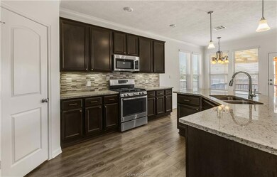 Kitchen with stainless steel appliances, dark brown cabinetry, pendant lighting, light stone counters, and crown molding