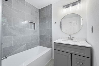 This modern bathroom features elegant gray tile walls, a sleek white bathtub, and a stylish vanity with a marble countertop. A round mirror and contemporary lighting add a touch of sophistication.
