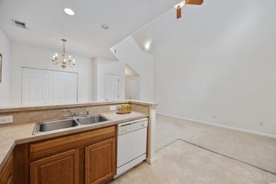 Kitchen with white dishwasher, light colored carpet, a chandelier, brown cabinets, and decorative light fixtures