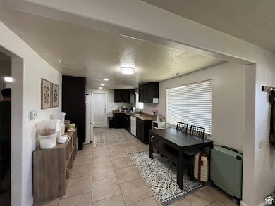 Kitchen featuring dark cabinetry, radiator, white appliances, light tile patterned floors, and a textured ceiling