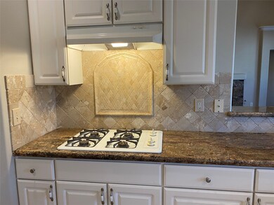 The kitchen has travertine backsplashes and a gas cooktop.
