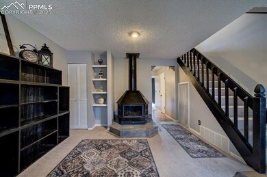 Unfurnished living room featuring light colored carpet, a textured ceiling, a wood stove, and stairway