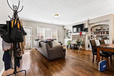 Living room with a textured ceiling, dark wood-style floors, built in features, crown molding, and a stone fireplace