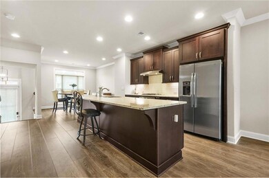 Kitchen featuring a breakfast bar, dark brown cabinets, stainless steel refrigerator with ice dispenser, light stone countertops, and a center island with sink