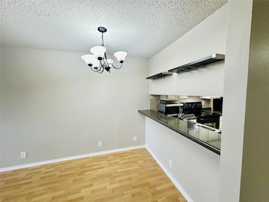 Kitchen featuring light wood-style floors, a chandelier, black range with electric stovetop, a textured ceiling, and pendant lighting