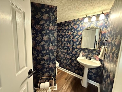 Half bathroom featuring wood finished floors, wallpapered walls, and a textured ceiling