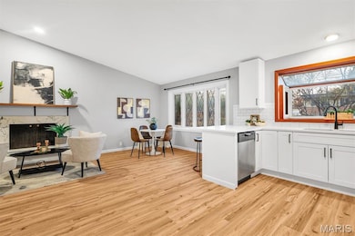 Kitchen featuring a high end fireplace, light wood finished floors, backsplash, a kitchen breakfast bar, and white cabinets