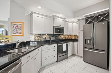 Kitchen featuring appliances with stainless steel finishes, a sink, backsplash, light tile patterned floors, and dark stone counters