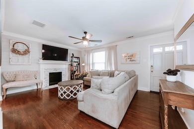 Living room featuring ceiling fan, ornamental molding, dark wood-style flooring, a fireplace with flush hearth, and baseboards
