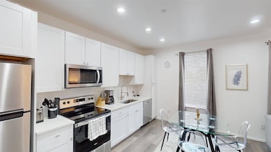 Kitchen with appliances with stainless steel finishes, white cabinets, light wood-style floors, decorative backsplash, and recessed lighting