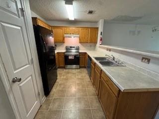 Kitchen featuring brown cabinetry, stainless steel range with electric cooktop, freestanding refrigerator, a peninsula, and light countertops