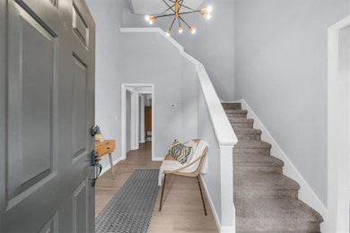 Foyer entrance featuring a high ceiling, light wood-type flooring, a chandelier, stairs, and baseboards