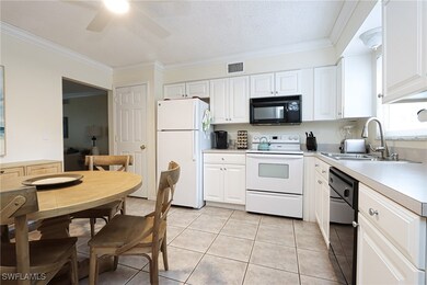 Kitchen with black appliances, light tile patterned flooring, light countertops, white cabinetry, and crown molding