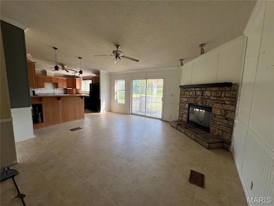 Unfurnished living room featuring ceiling fan, crown molding, a textured ceiling, a decorative wall, and a stone fireplace