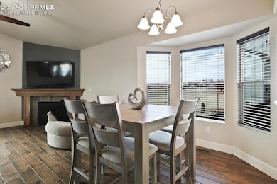 Dining room featuring dark wood-style floors, baseboards, a chandelier, a tile fireplace, and vaulted ceiling
