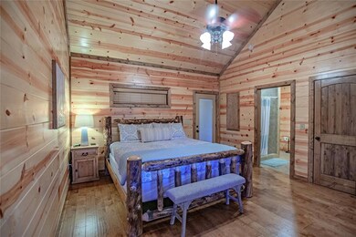 Bedroom with wood walls, light wood finished floors, high vaulted ceiling, ceiling fan, and wooden ceiling