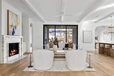 Dining space with arched walkways, light wood finished floors, a high end fireplace, ceiling fan, and beamed ceiling