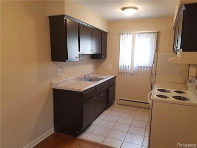 Kitchen with white appliances, light countertops, baseboard heating, dark brown cabinetry, and under cabinet range hood