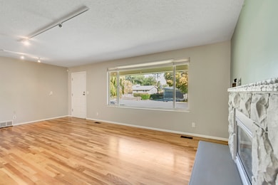 Unfurnished living room featuring a stone fireplace, track lighting, light wood-style flooring, and a textured ceiling