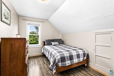 Bedroom with wood finished floors, baseboards, and vaulted ceiling