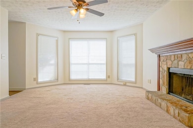 Unfurnished living room with carpet, a ceiling fan, a fireplace, a textured ceiling, and baseboards