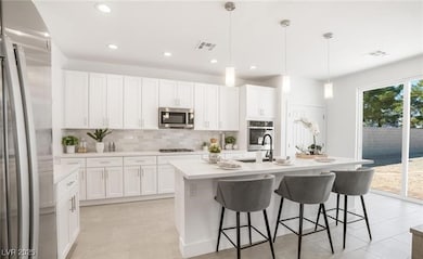 Kitchen with appliances with stainless steel finishes, decorative backsplash, pendant lighting, a kitchen breakfast bar, and white cabinets