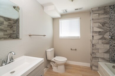 Full bathroom with light wood-style floors, vanity, and a textured wall