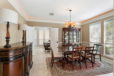 Spacious formal dining room with crown molding with up lighting, wainscoting and tile flooring.