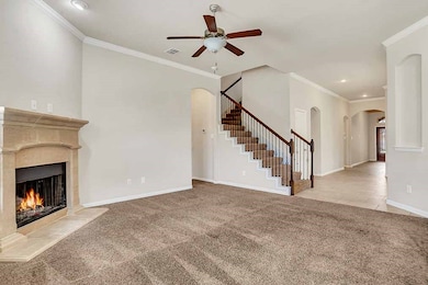 Living room featuring light colored carpet, crown molding, a fireplace, arched walkways, and stairway