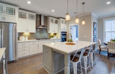 Kitchen featuring decorative backsplash, appliances with stainless steel finishes, wall chimney exhaust hood, dark wood finished floors, and a kitchen island with sink
