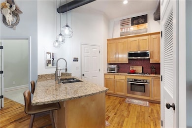 Kitchen with stainless steel appliances, light wood finished floors, tasteful backsplash, light stone countertops, and a high ceiling