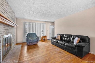 Living room featuring wood finished floors, a textured ceiling, and a brick fireplace