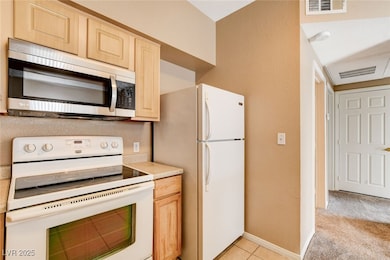 Kitchen featuring white appliances, light countertops, light brown cabinetry, light tile patterned floors, and a textured wall