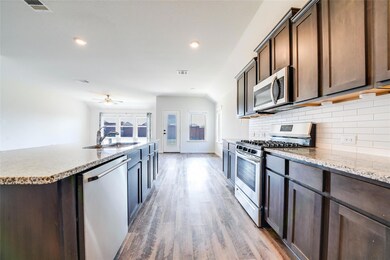 Kitchen with appliances with stainless steel finishes, decorative backsplash, a center island with sink, hardwood / wood-style floors, and sink