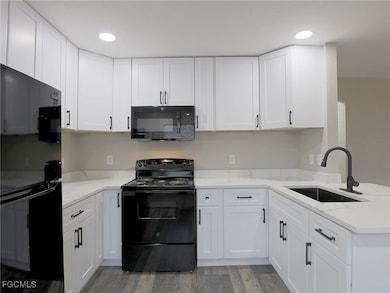 Kitchen featuring black appliances, white cabinets, light wood-style flooring, recessed lighting, and light stone countertops