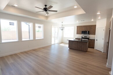 Kitchen with open floor plan, a raised ceiling, dark countertops, an island with sink, and light wood-style floors