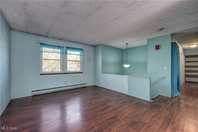 Spare room featuring a baseboard heating unit, dark wood-type flooring, and a textured ceiling