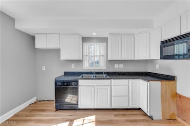 Kitchen with dark countertops, black appliances, white cabinets, light wood-style flooring, and recessed lighting