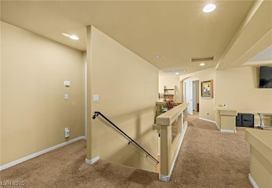 Hallway with an upstairs landing, light colored carpet, arched walkways, and recessed lighting