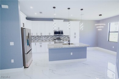 Kitchen with light marble finish floors, tasteful backsplash, stainless steel appliances, hanging light fixtures, and white cabinetry
