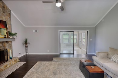 Living area with ornamental molding, a stone fireplace, wood finished floors, a ceiling fan, and baseboards