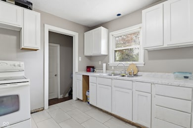 kitchen with white electric range, light countertops, white cabinets, and light tile patterned flooring